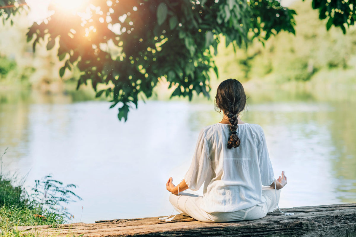 A woman meditating by a lake at a wellness retreat